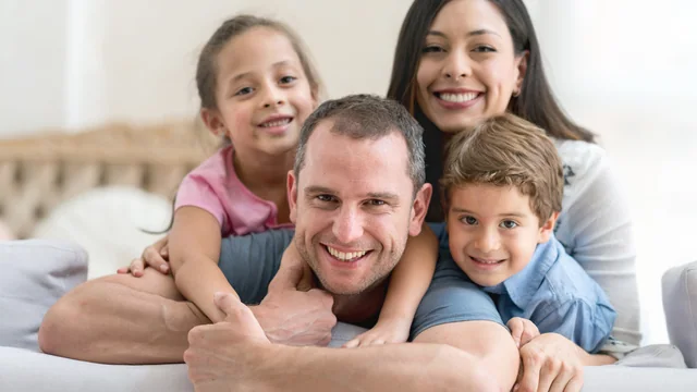 Pai, mãe e dois filhos juntos, sorrindo em casa.